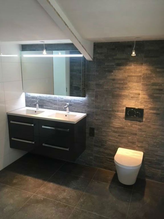 Badkamer met dubbel wastafelmeubel, verlichte spiegel en natuursteen wand in Spierdijk