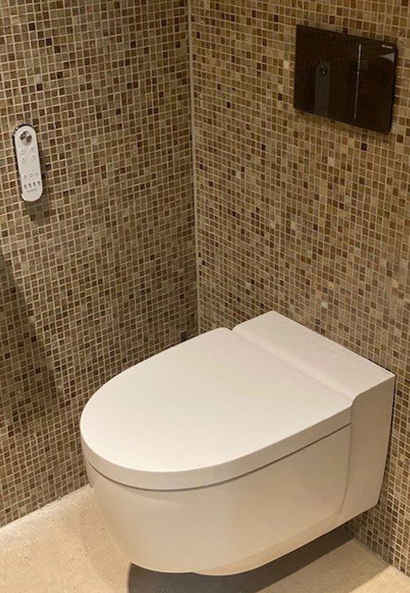 Hangend douchetoilet tegen beige mozaïektegels in gerenoveerde badkamer in Amstelveen