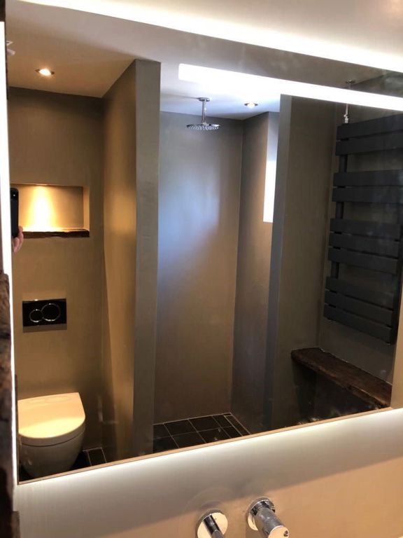 Spiegelbeeld van badkamer met regendouche, hangtoilet en zwarte handdoekradiator in Hoorn