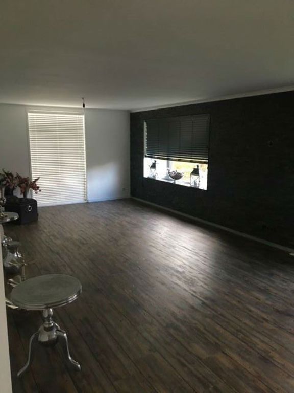 Woonkamer met donkere houten vloer en zwarte accentwand na renovatie in Spierdijk